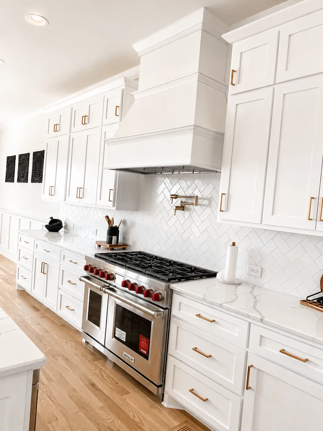 White kitchen cabinetry with brass pulls, herringbone tile, and a professional range