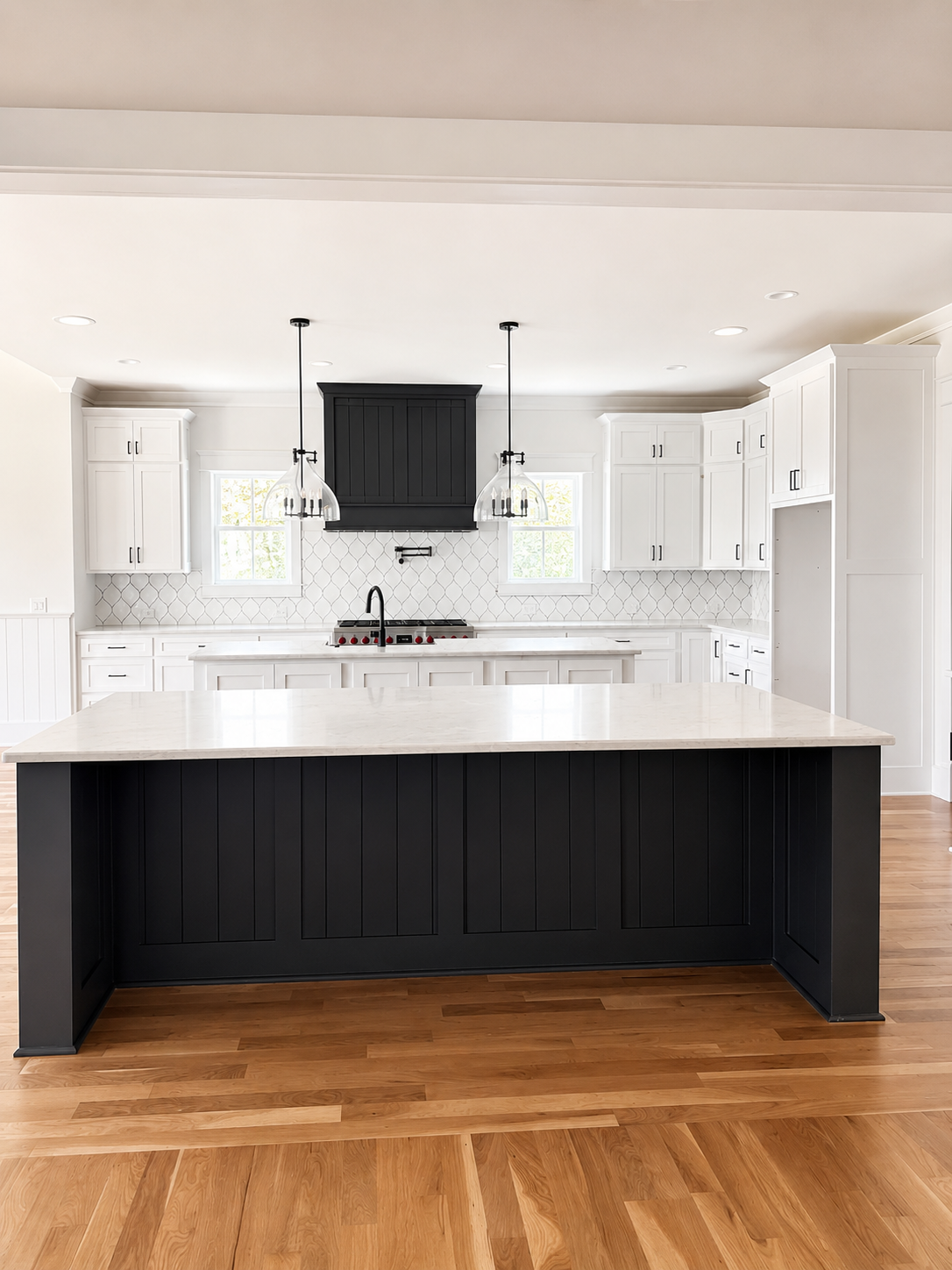 White kitchen cabinetry with a black board-and-batten island and matching range hood